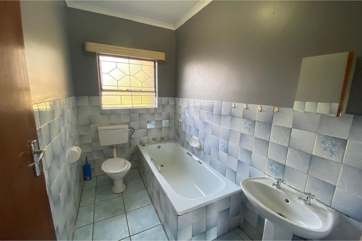 A functional bathroom featuring a standard bathtub, pedestal basin, and toilet with dated blue and white wall tiling.