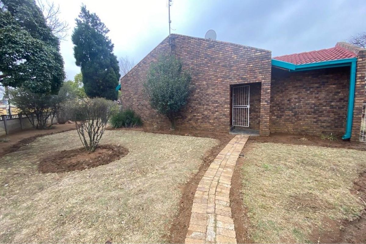 A view of the rear exterior of the house featuring a brick facade, a paved walkway, and a garden area.