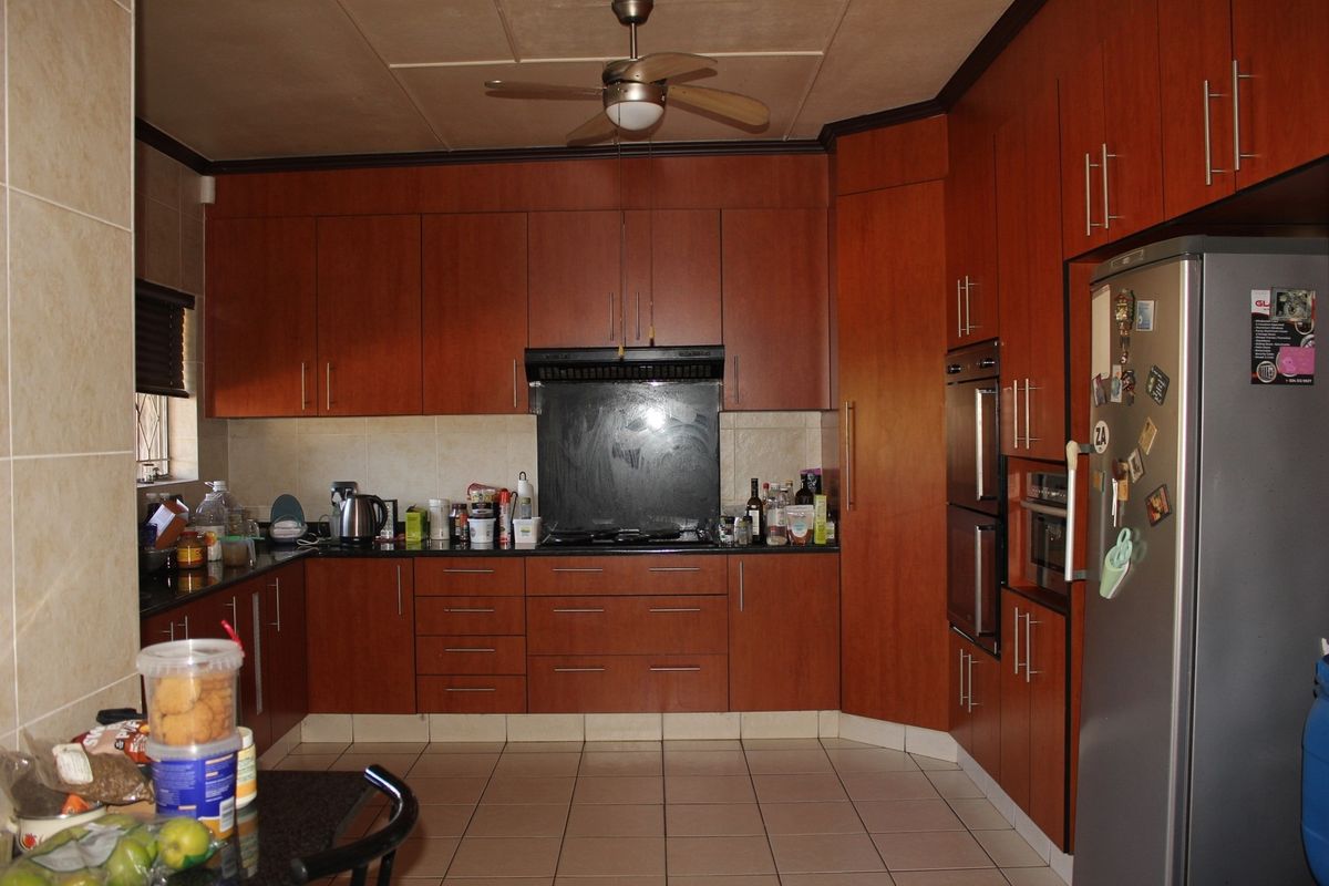 A functional kitchen featuring dark wood-veneer cabinetry, built-in double ovens, a hob with extractor fan, and tiled flooring.