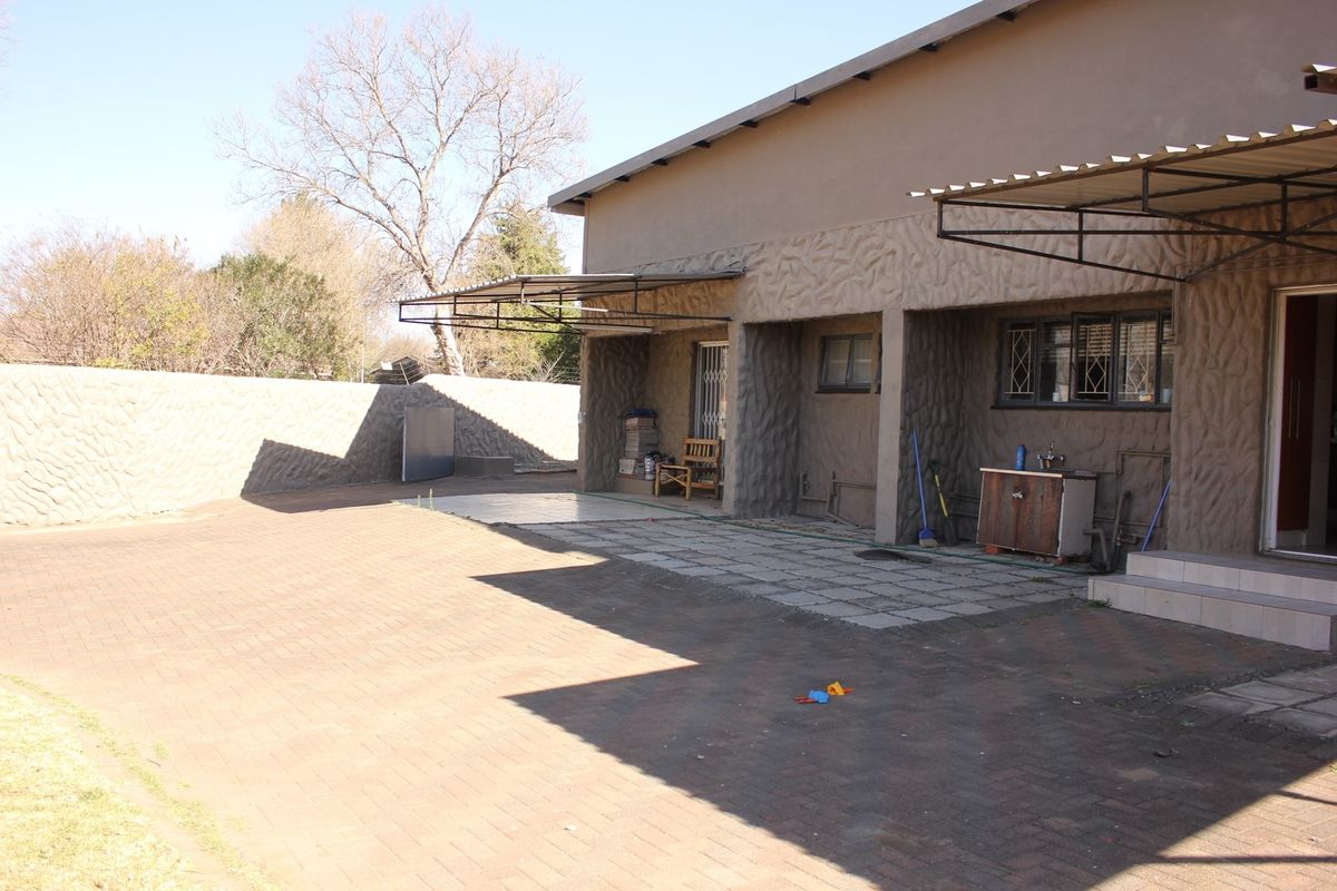 Rear exterior view featuring a paved courtyard, covered patio area, and textured wall finishes.