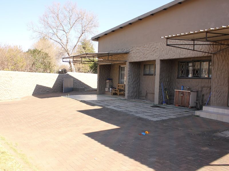 Rear exterior view featuring a paved courtyard, covered patio area, and textured wall finishes.