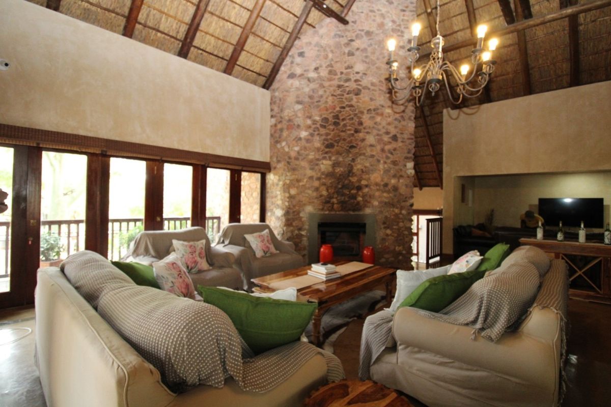 Spacious living room featuring a high vaulted thatched ceiling with exposed rafters, a prominent stone fireplace, and large wooden-framed glass doors.