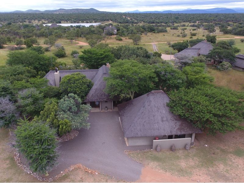 Aerial view of a property featuring multiple structures with traditional thatch roofs, surrounded by natural bushveld landscape and a gravel driveway.
