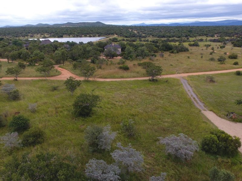 An aerial view of the expansive natural landscape, featuring dirt access roads and a nearby water body within a rural estate setting.