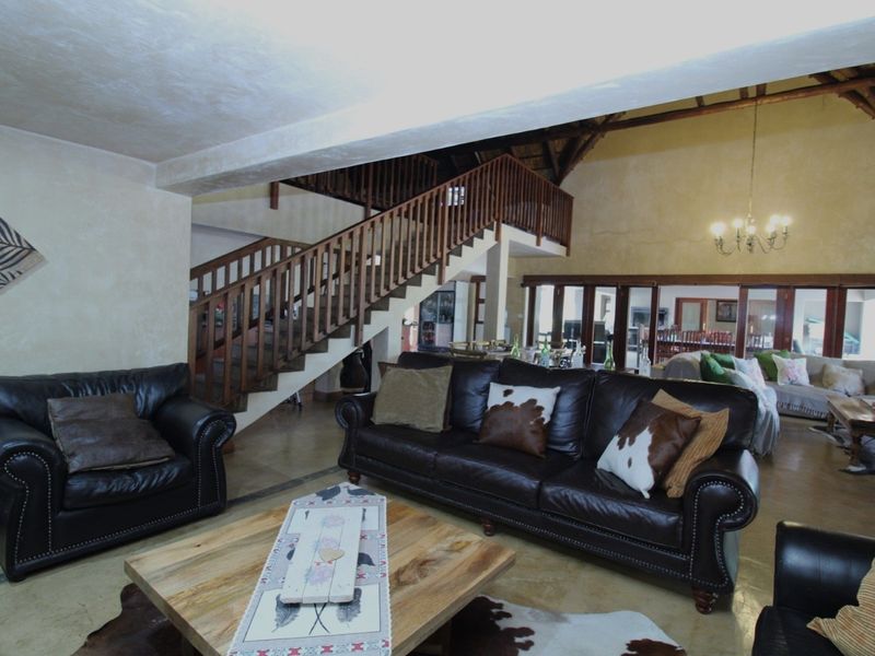 Spacious open-plan living area featuring a prominent wooden staircase, vaulted ceilings with exposed timber beams, and large sliding glass doors leading to the exterior.
