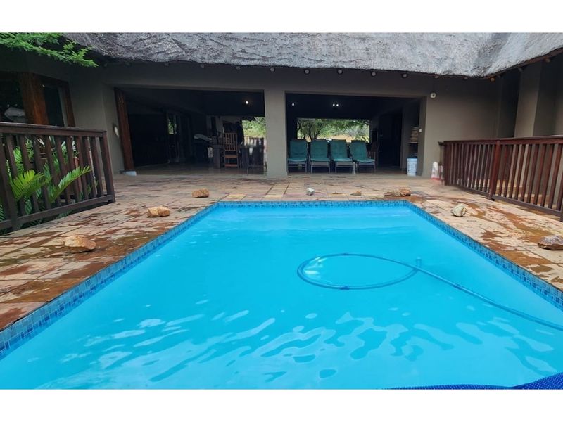 Outdoor pool area featuring a swimming pool, tiled patio, and a covered veranda with a thatched roof structure.