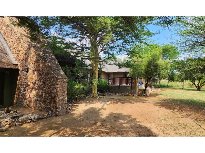 Rear view of the property featuring a thatched roof, stone-clad exterior walls, and a raised patio area overlooking the garden.