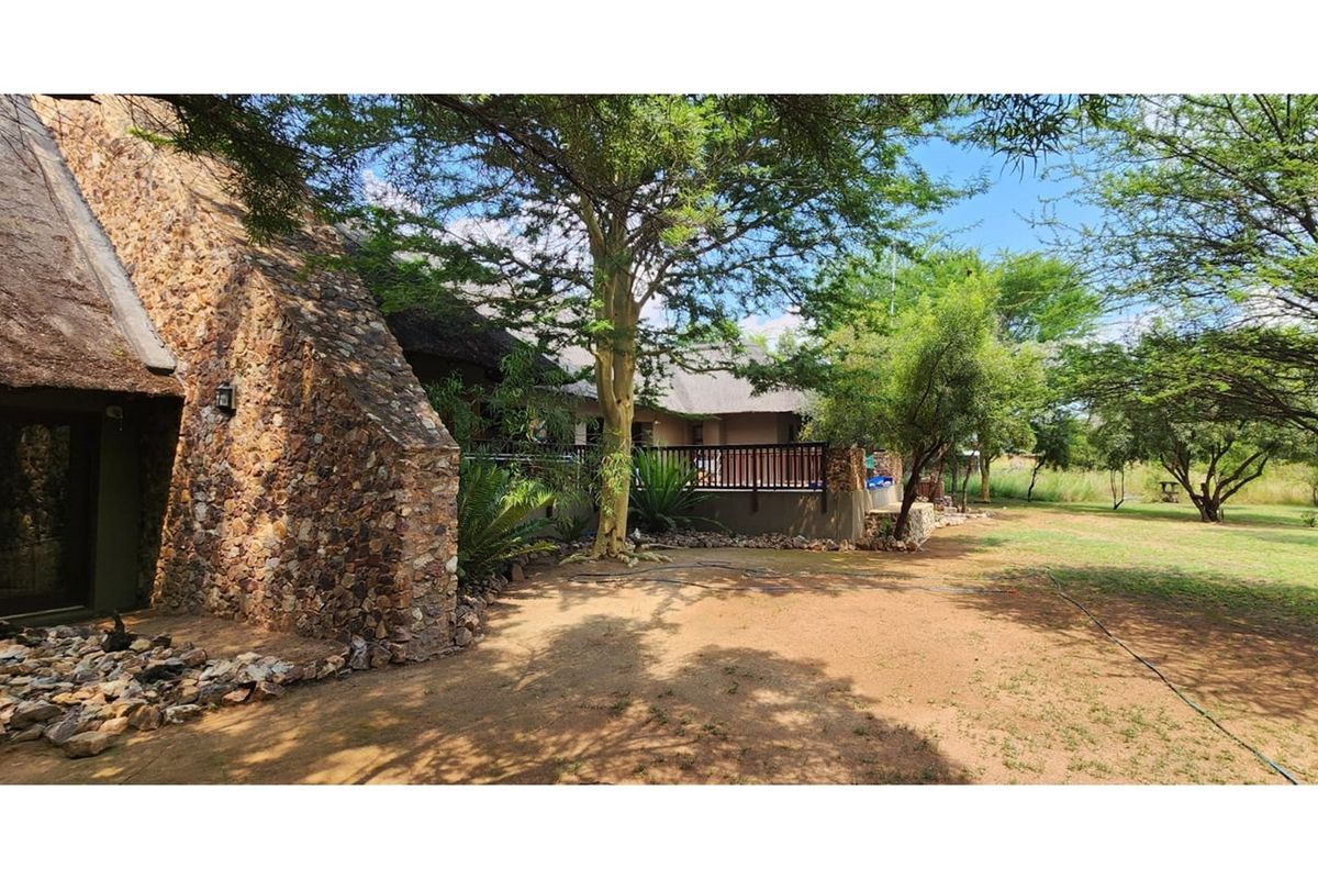 Rear view of the property featuring a thatched roof, stone-clad exterior walls, and a raised patio area overlooking the garden.