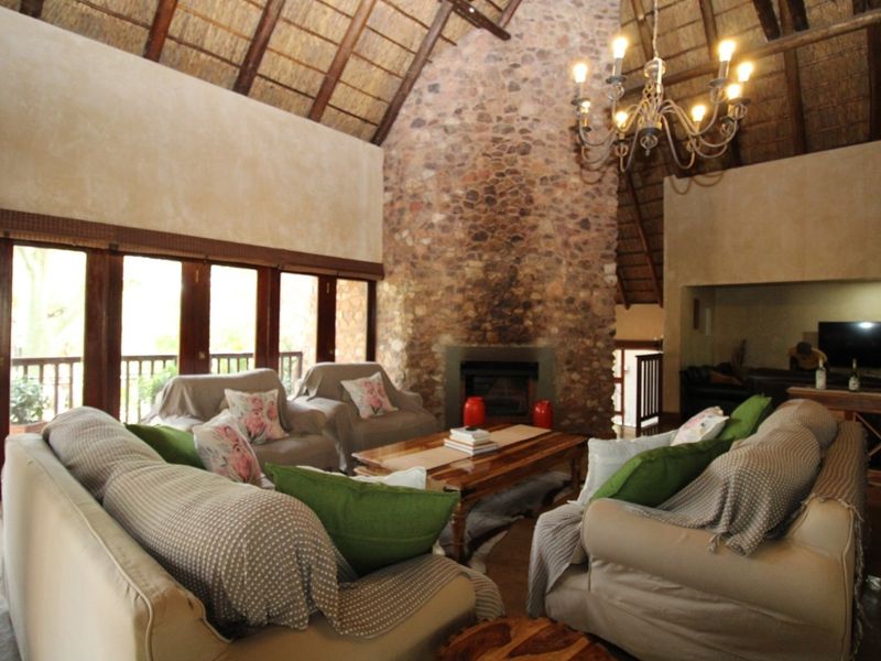 Spacious living room featuring a high vaulted thatched ceiling with exposed rafters, a prominent stone fireplace, and large wooden-framed glass doors.