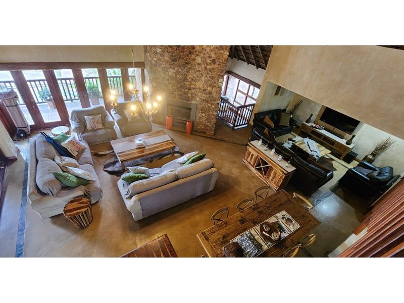 Spacious open-plan living area featuring a striking stone fireplace, polished concrete floors, and high double-volume ceilings with exposed timber beams.
