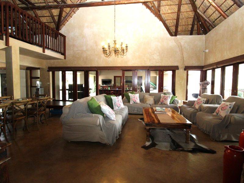 Spacious open-plan living area featuring a high vaulted thatched ceiling with exposed timber trusses, concrete floors, and a mezzanine level overlooking the space.