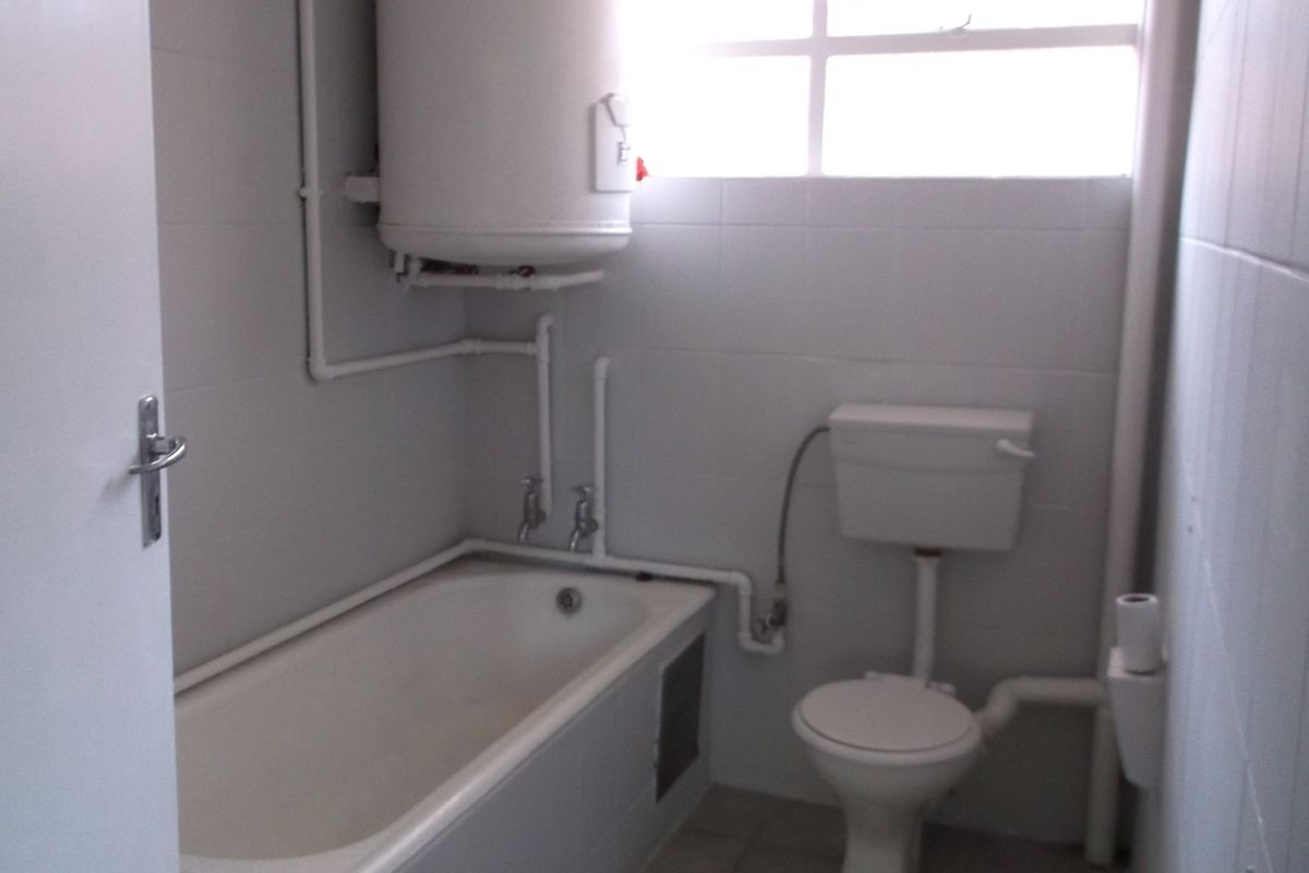 A functional bathroom featuring a standard bathtub, toilet, and wall-mounted electric water heater with visible plumbing fixtures.