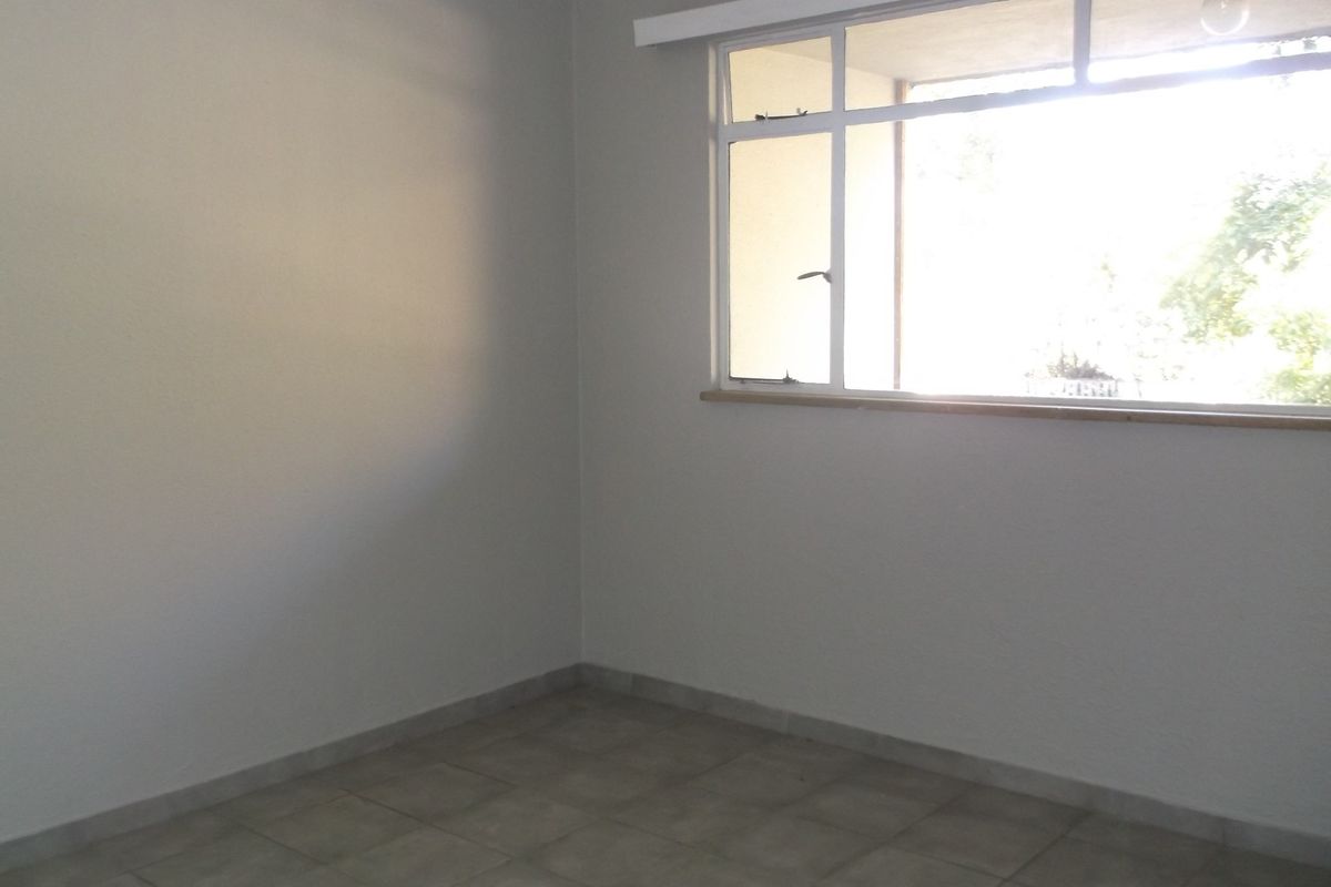A bright, empty bedroom featuring neutral tiled flooring and a large window, providing a clean canvas for personalization.