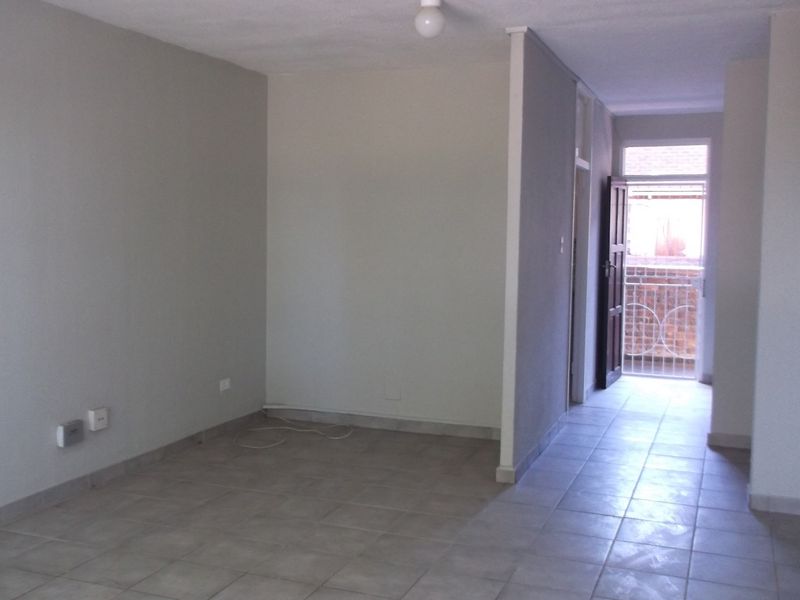 An empty, neutrally painted living area featuring tiled flooring and direct access to an exterior balcony through a security gate.