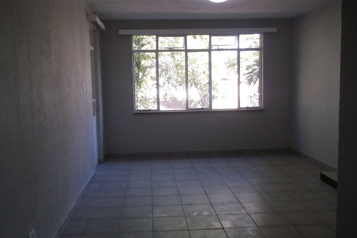 An empty, neutrally finished living room featuring tiled flooring and a large window providing natural light.