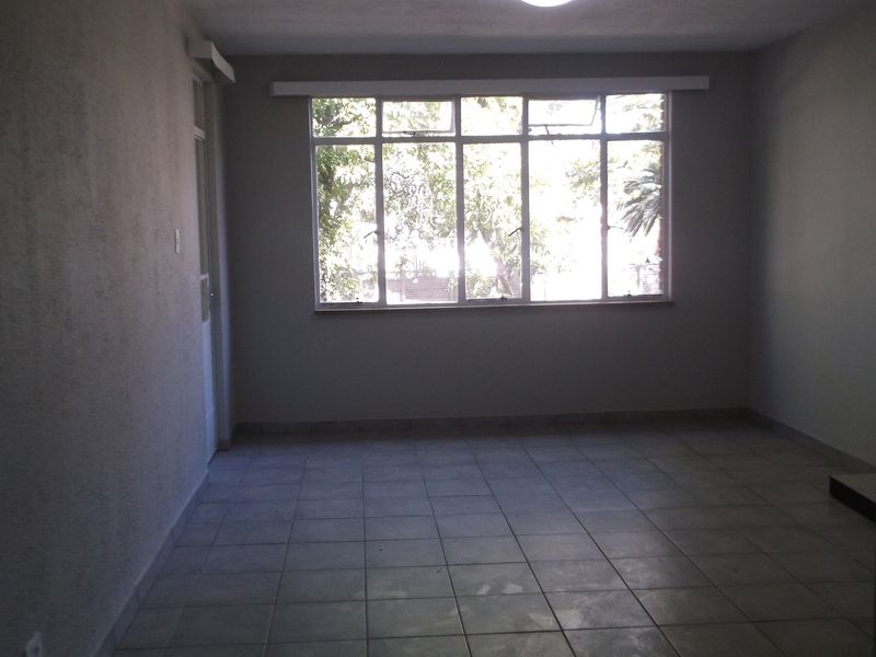 An empty, neutrally finished living room featuring tiled flooring and a large window providing natural light.
