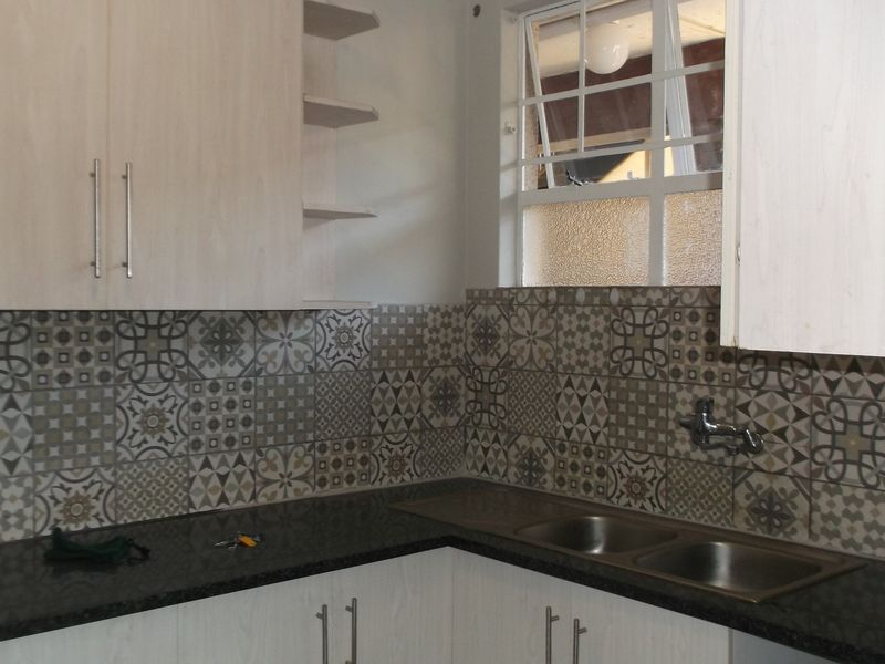 A functional kitchen area featuring light-toned cabinetry, dark granite countertops, a double stainless steel sink, and decorative patterned tile backsplash.
