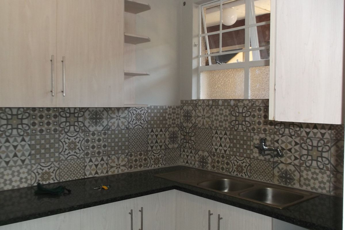 A functional kitchen area featuring light-toned cabinetry, dark granite countertops, a double stainless steel sink, and decorative patterned tile backsplash.