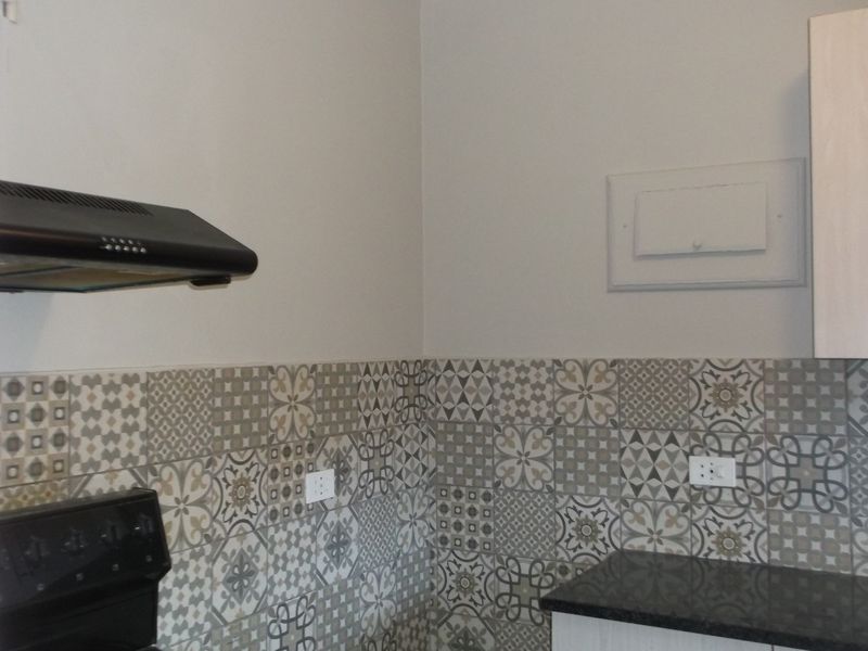 A clean kitchen area featuring a patterned tile backsplash, dark granite countertops, built-in cabinetry, and a wall-mounted extractor fan.