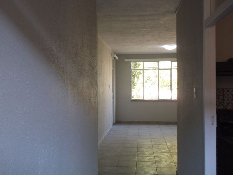 A vacant hallway with tiled flooring and a large window, showing signs of wall staining and requiring cosmetic attention.