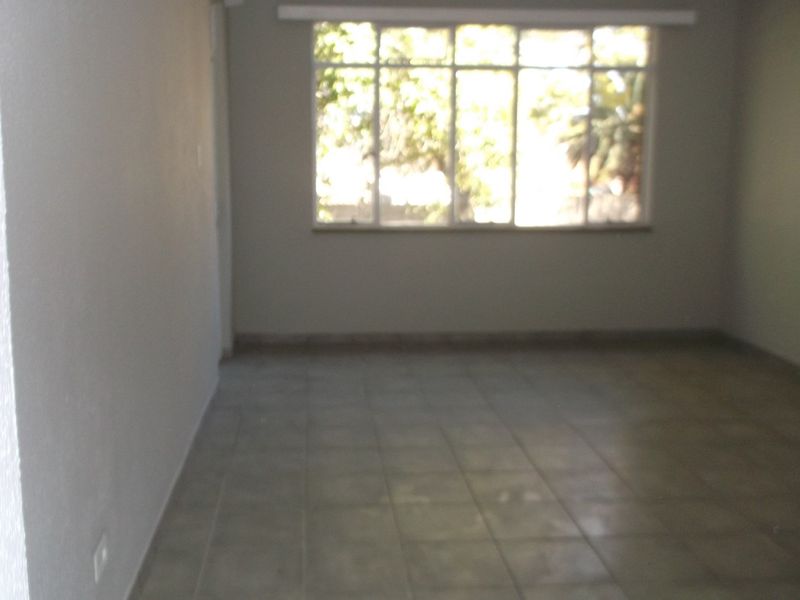 An empty, neutrally painted living area featuring tiled flooring and a large window that allows for natural light.
