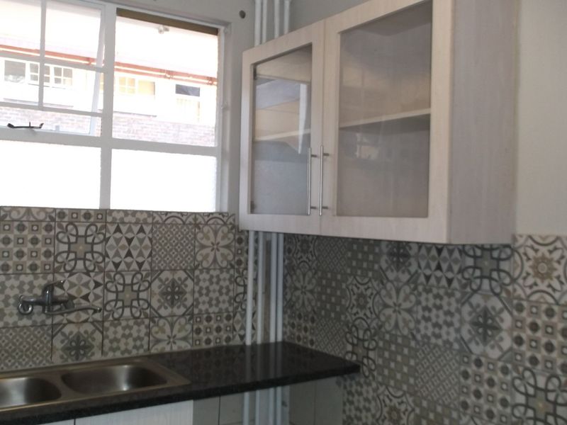 A clean kitchen area featuring patterned wall tiles, a double bowl stainless steel sink, granite countertops, and wall-mounted glass-fronted cabinetry.