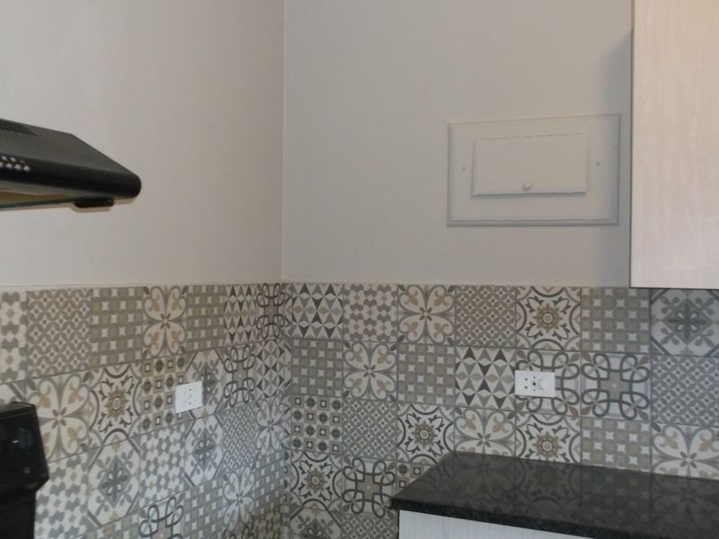 A clean kitchen corner featuring a patterned tile backsplash, granite countertop, and a built-in extractor fan.