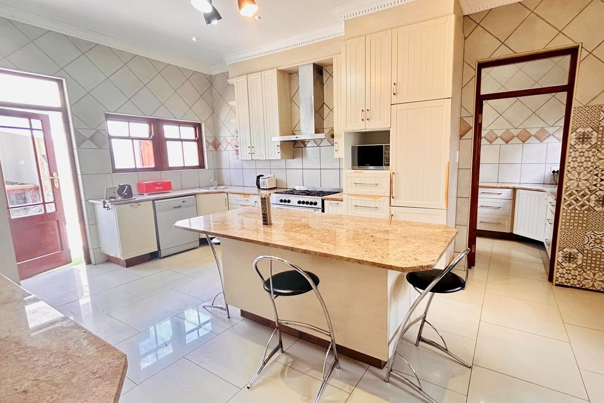 Spacious kitchen featuring a central island with granite countertop, built-in oven, extractor fan, and tiled flooring, with an adjacent scullery area.