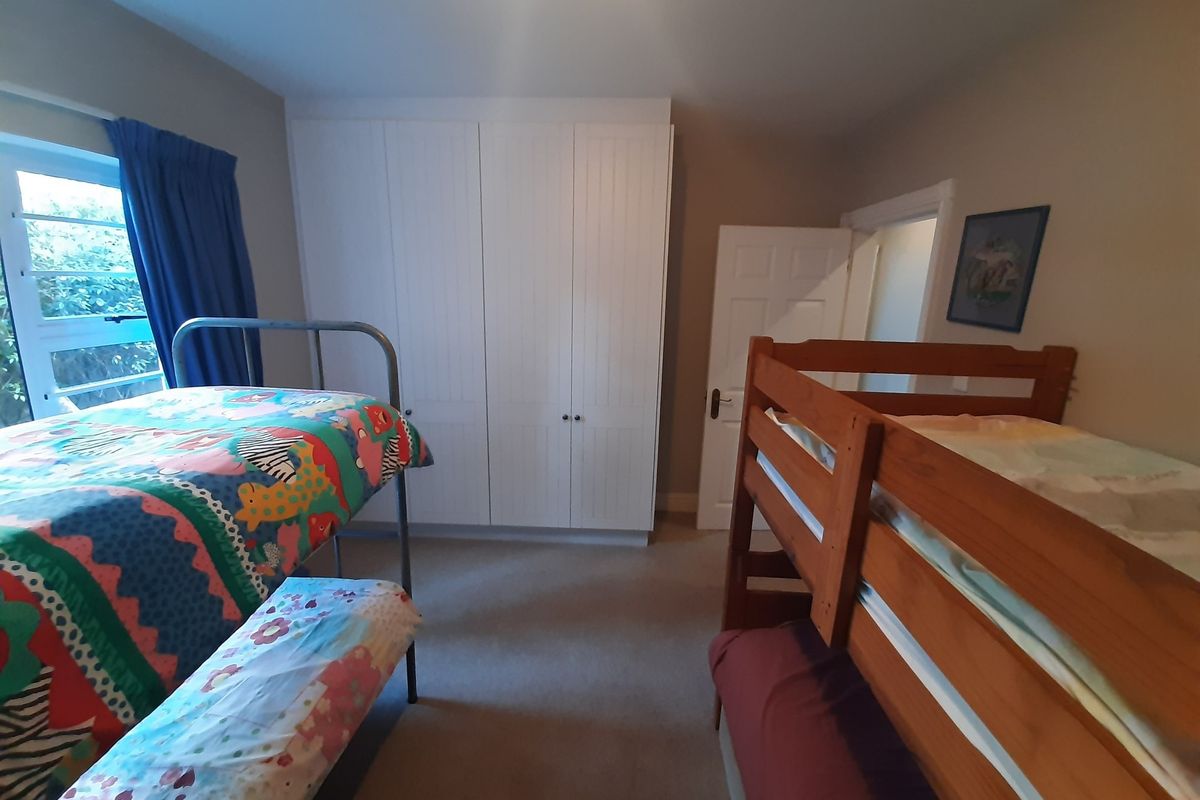 A functional bedroom featuring a large white built-in wardrobe and a window providing natural light.