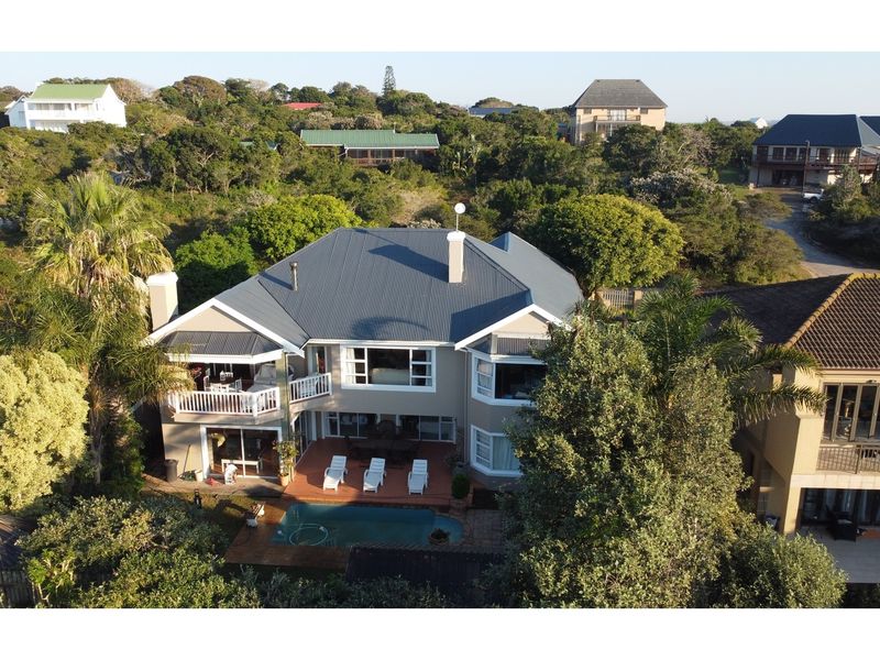 Aerial view of a residential property featuring a swimming pool, rear deck, balcony, and a corrugated metal roof set within a landscaped garden.