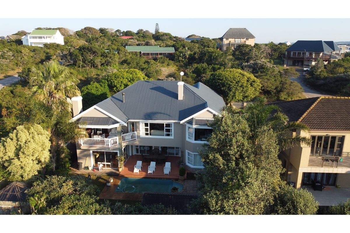 Aerial view of a residential property featuring a swimming pool, rear deck, balcony, and a corrugated metal roof set within a landscaped garden.