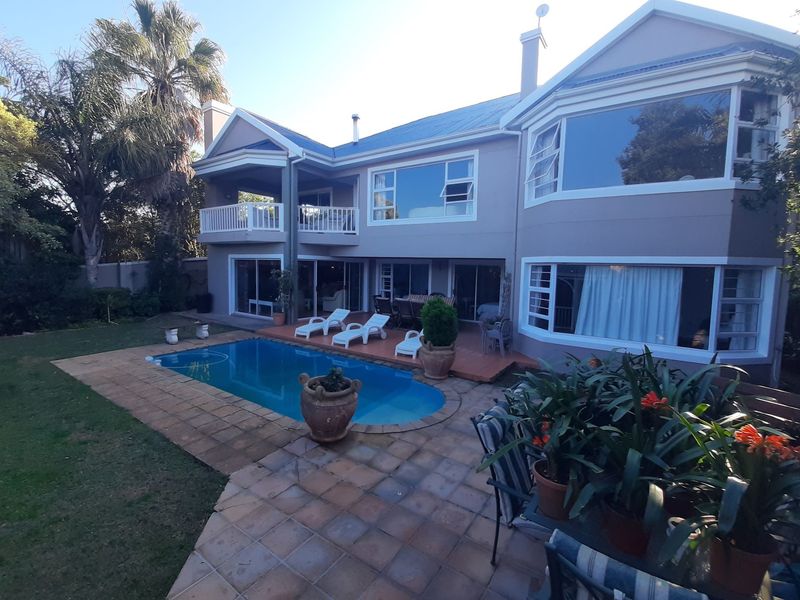 Rear view of a two-story house featuring a swimming pool, paved patio area, upper-level balcony, and large windows overlooking the garden.