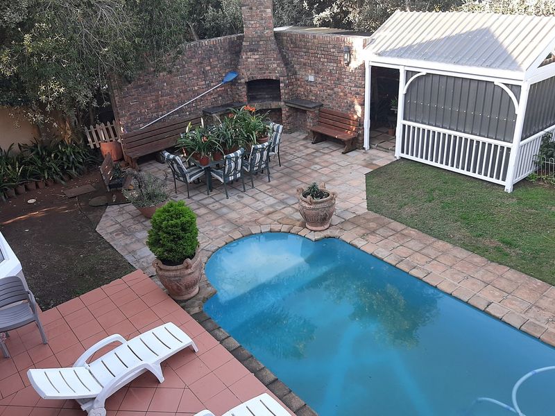 Outdoor entertainment area featuring a swimming pool, paved patio, and a brick built-in braai, complemented by a garden gazebo.