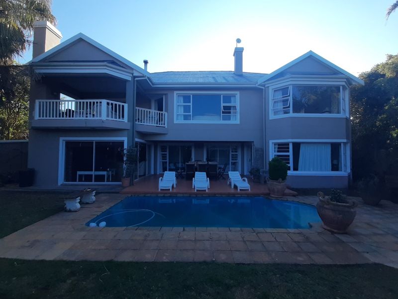 Rear view of a two-story house featuring a swimming pool, paved patio area, and an upper-level balcony.