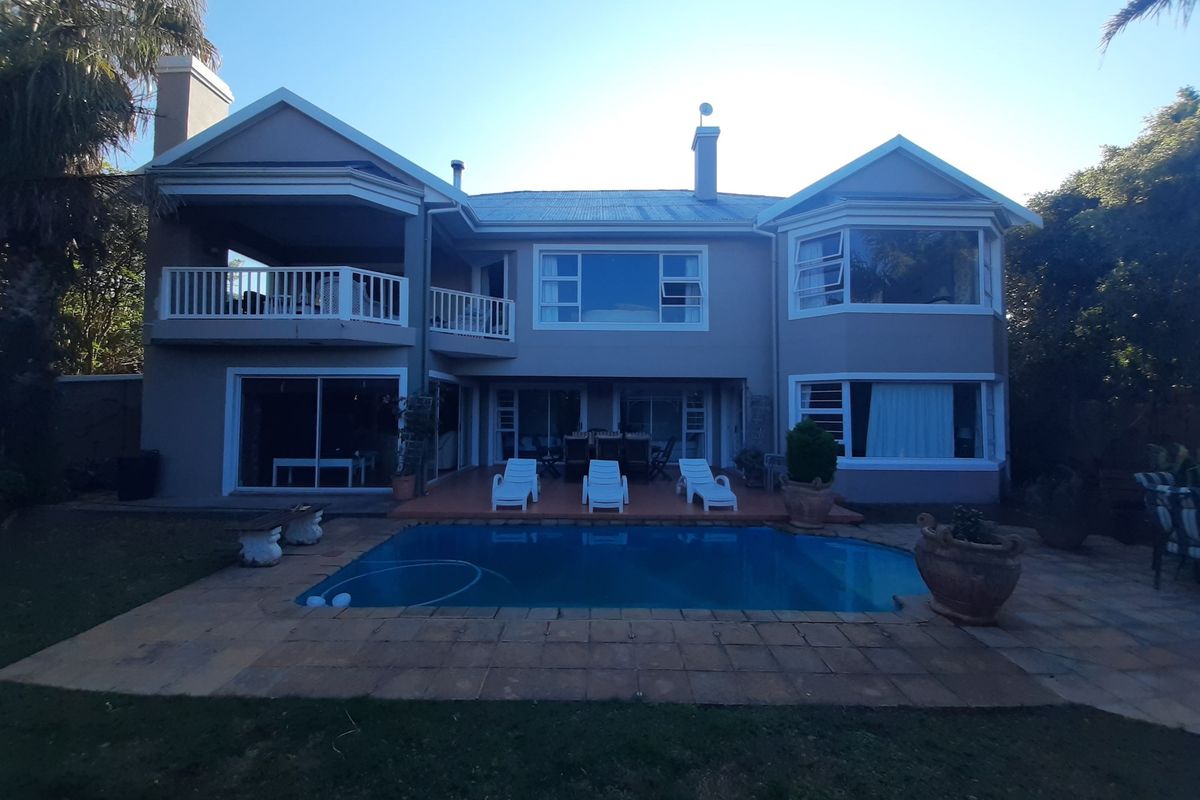 Rear view of a two-story house featuring a swimming pool, paved patio area, and an upper-level balcony.