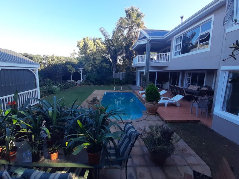 Rear view of a two-story house featuring a swimming pool, tiled patio area, upper-level balcony, and a garden gazebo.