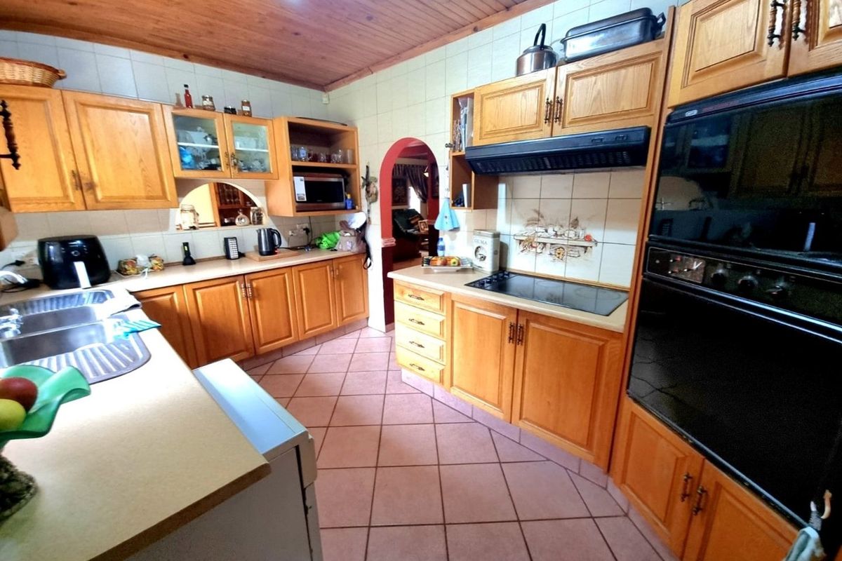 A functional kitchen featuring wooden cabinetry, built-in oven, electric hob, extractor fan, and tiled flooring with a classic layout.