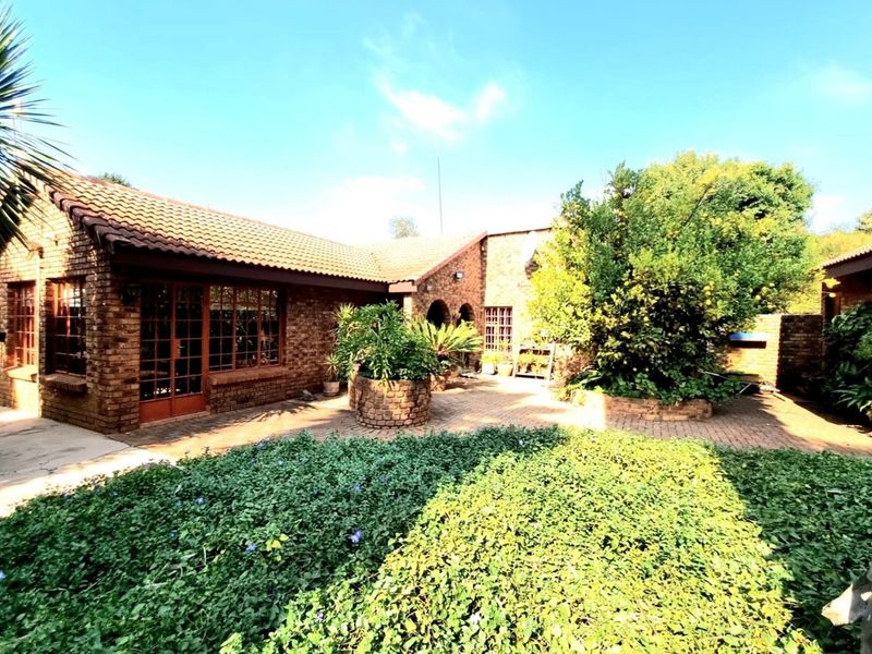 A charming brick-built farmhouse exterior featuring a paved courtyard, established garden beds, and classic tiled roofing.