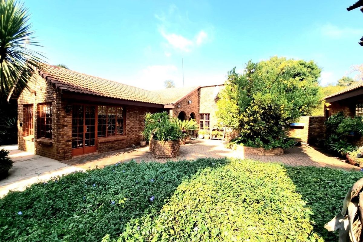 A charming brick-built farmhouse exterior featuring a paved courtyard, established garden beds, and classic tiled roofing.