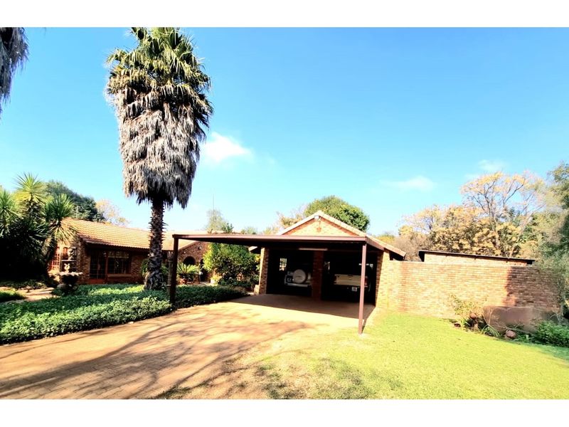 A view of the farm property featuring a brick-built double carport, paved driveway, and established garden surroundings.