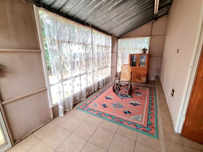 A sunroom or enclosed patio area featuring tiled flooring, large windows, and a corrugated metal roof structure.