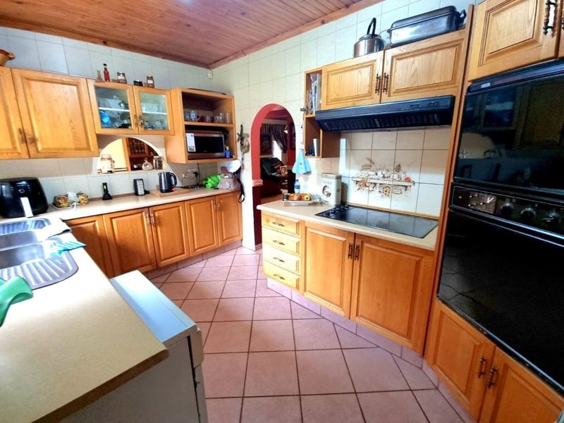 A functional kitchen featuring wooden cabinetry, built-in oven, electric hob, extractor fan, and tiled flooring with a classic layout.