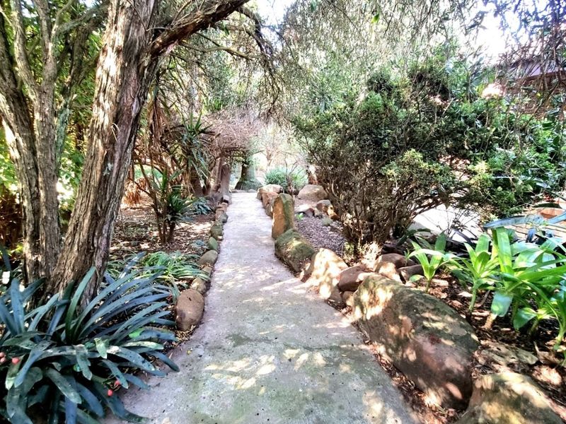 A landscaped garden pathway featuring natural stone borders and mature trees, providing a scenic walkway through the property grounds.