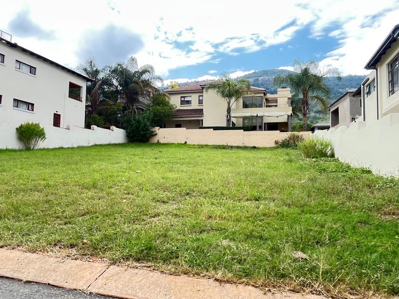 A vacant residential plot of land situated between existing multi-story homes, featuring a grassed surface and perimeter boundary walls.