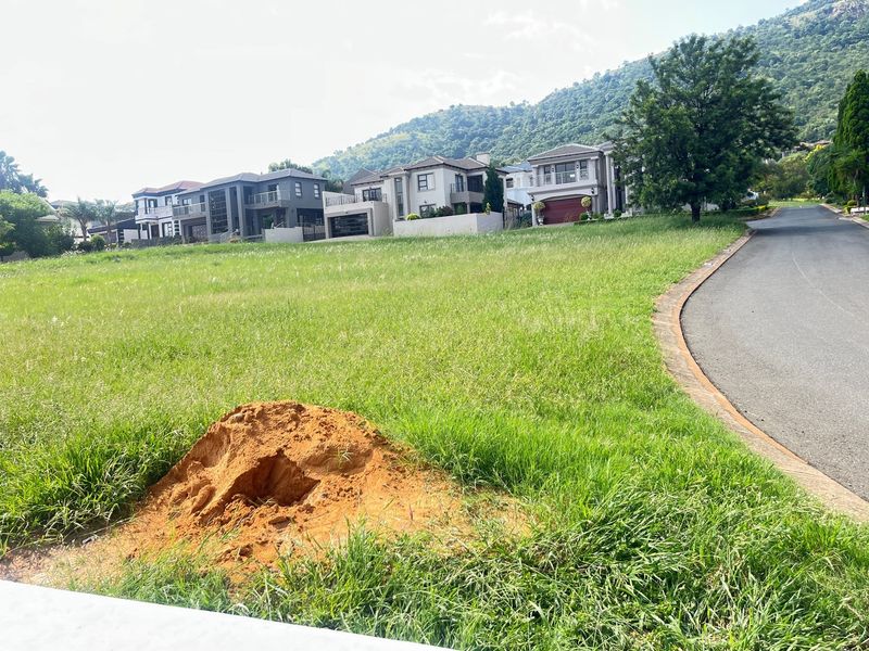 A vacant residential plot situated in a developed estate, featuring established surrounding homes and paved road access.