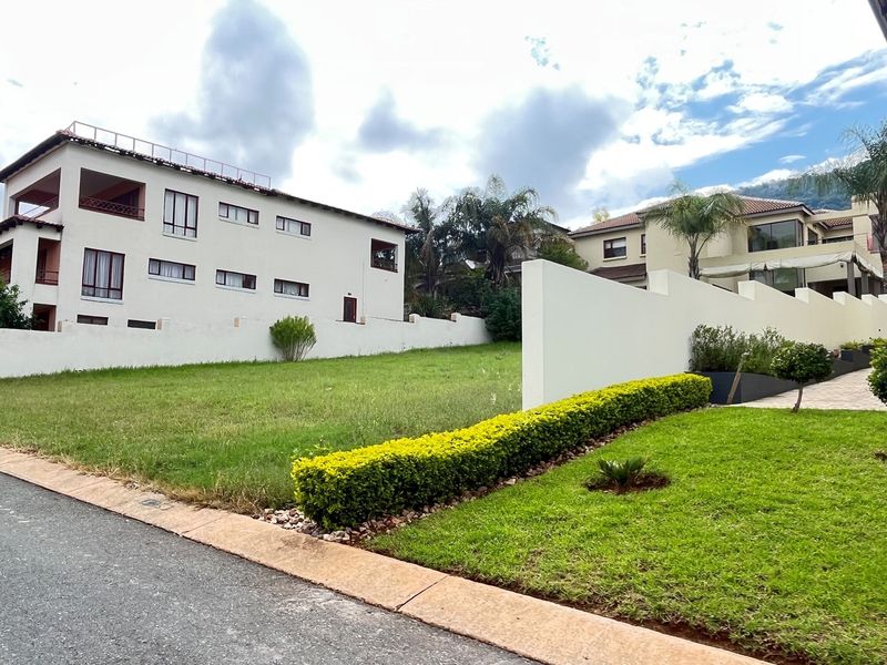 A view of a vacant residential plot featuring manicured lawn, established hedge landscaping, and a perimeter boundary wall in a residential estate setting.