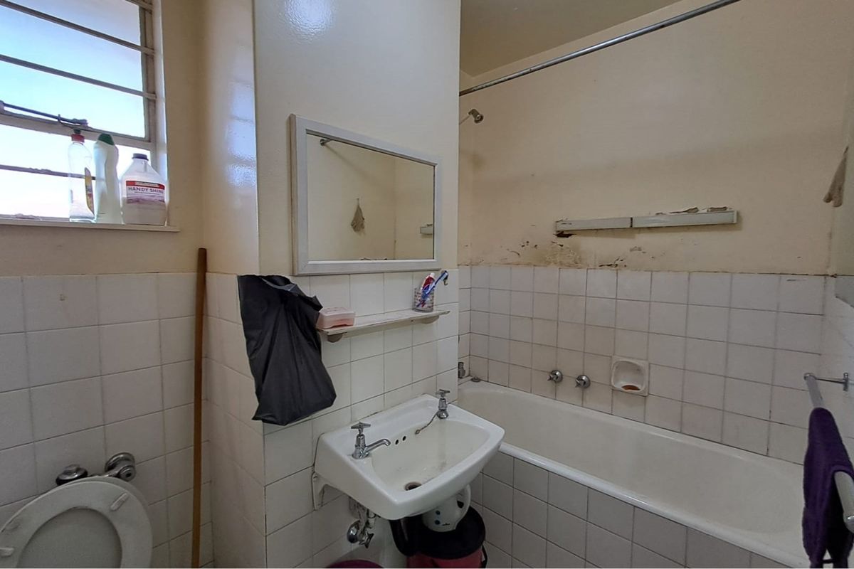 A dated bathroom featuring a standard bathtub, wall-mounted basin, and tiled splashbacks, currently requiring cosmetic renovation and wall repairs.