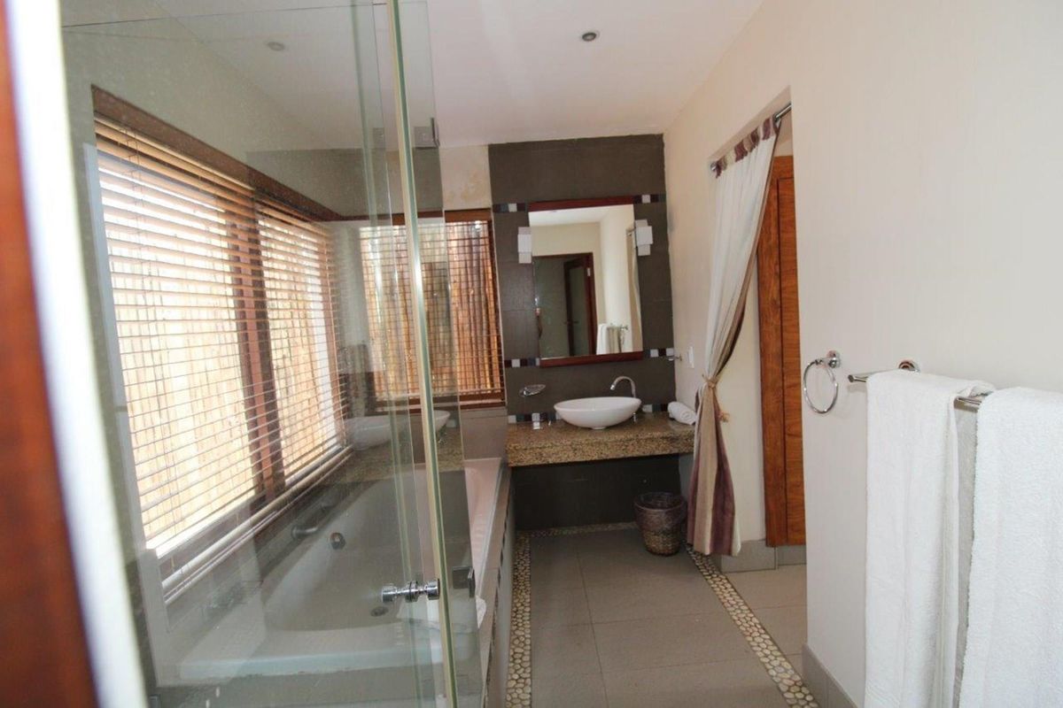 A functional bathroom featuring a built-in vanity with a vessel sink, a glass-enclosed shower, and a bathtub with wooden blinds.