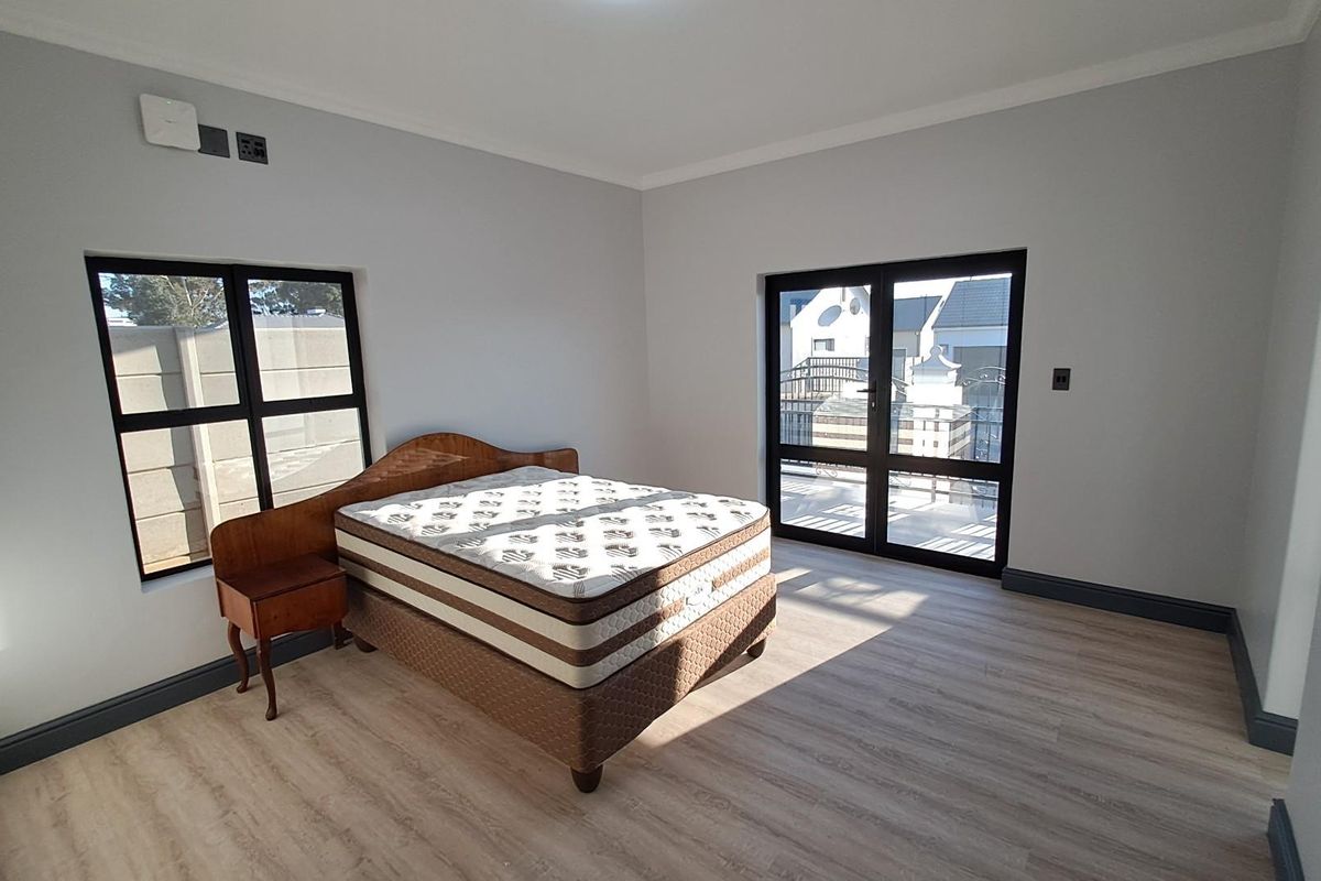 A bright and spacious bedroom featuring modern light wood-look flooring, dark-framed windows, and a glass door leading to an outdoor area.