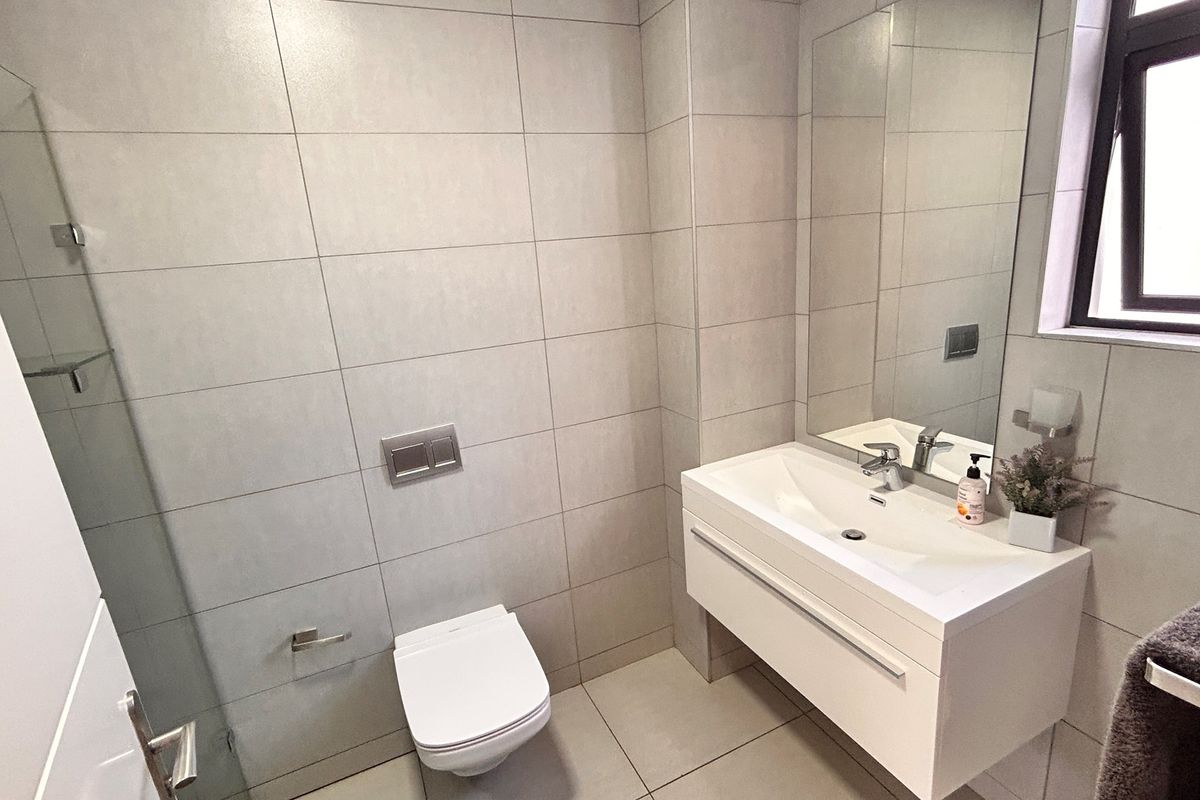 Modern bathroom featuring a wall-mounted vanity with integrated basin, large wall mirror, and a concealed cistern toilet with tiled walls and flooring.